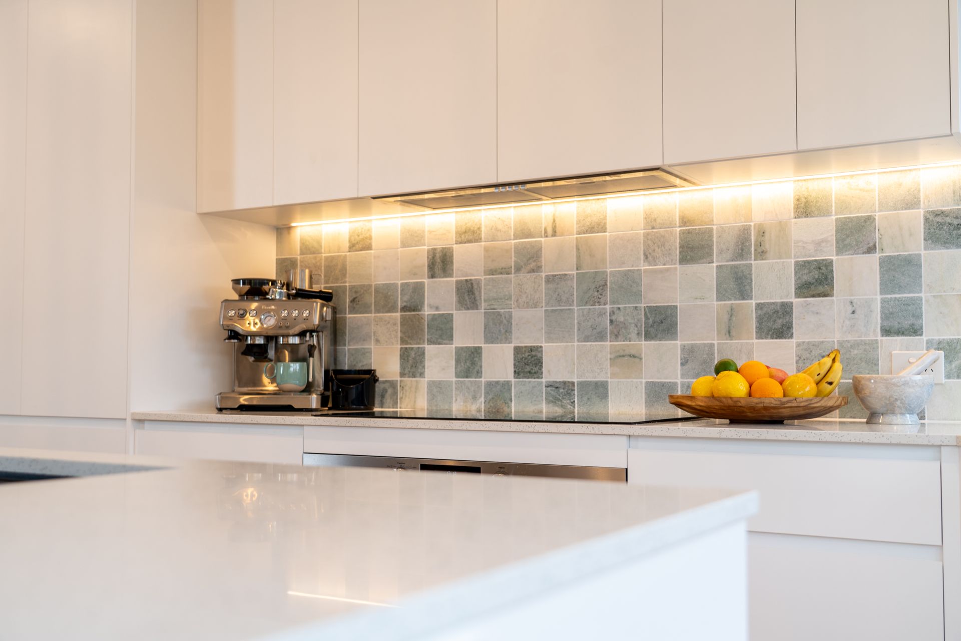 White kitchen with marble backsplash, espresso machine, fruit basket, and under-cabinet lighting