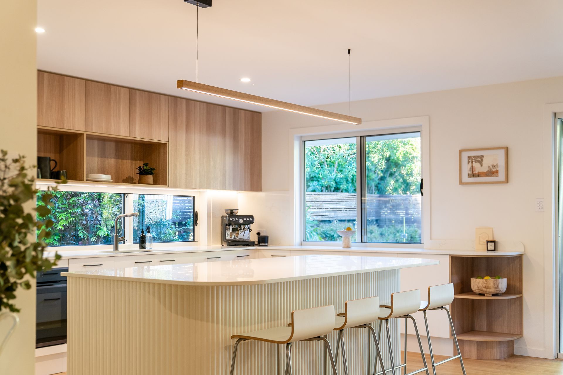 Modern kitchen with light wood cabinetry, white countertops, island with seating and window.