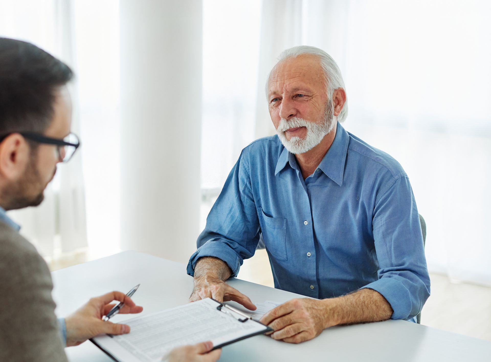 Man in blue shirt speaks to a person holding documents at a table. Bright  4= 0-p  room
