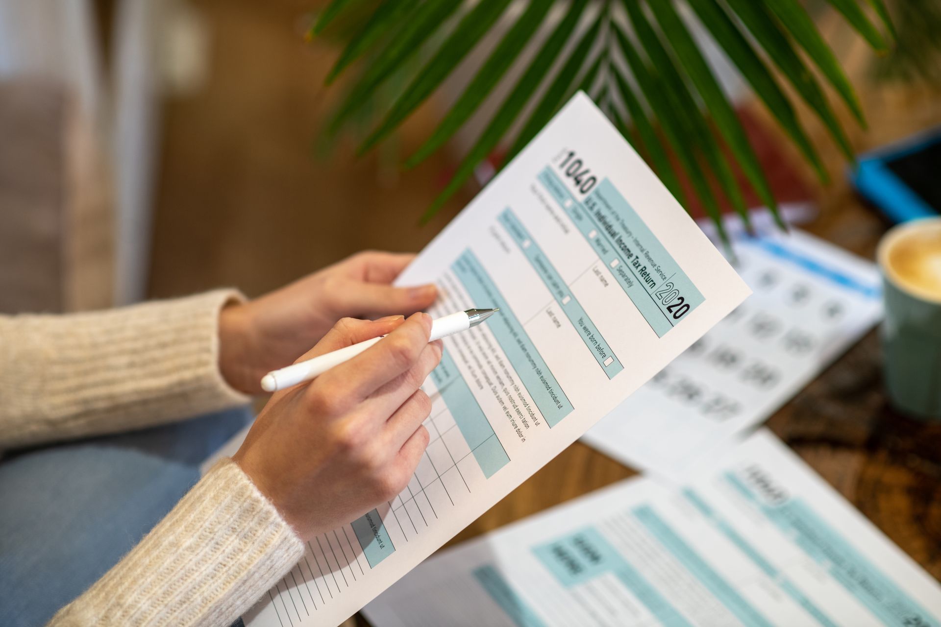 Person filling out tax form 1040, holding pen, palm leaf in background.