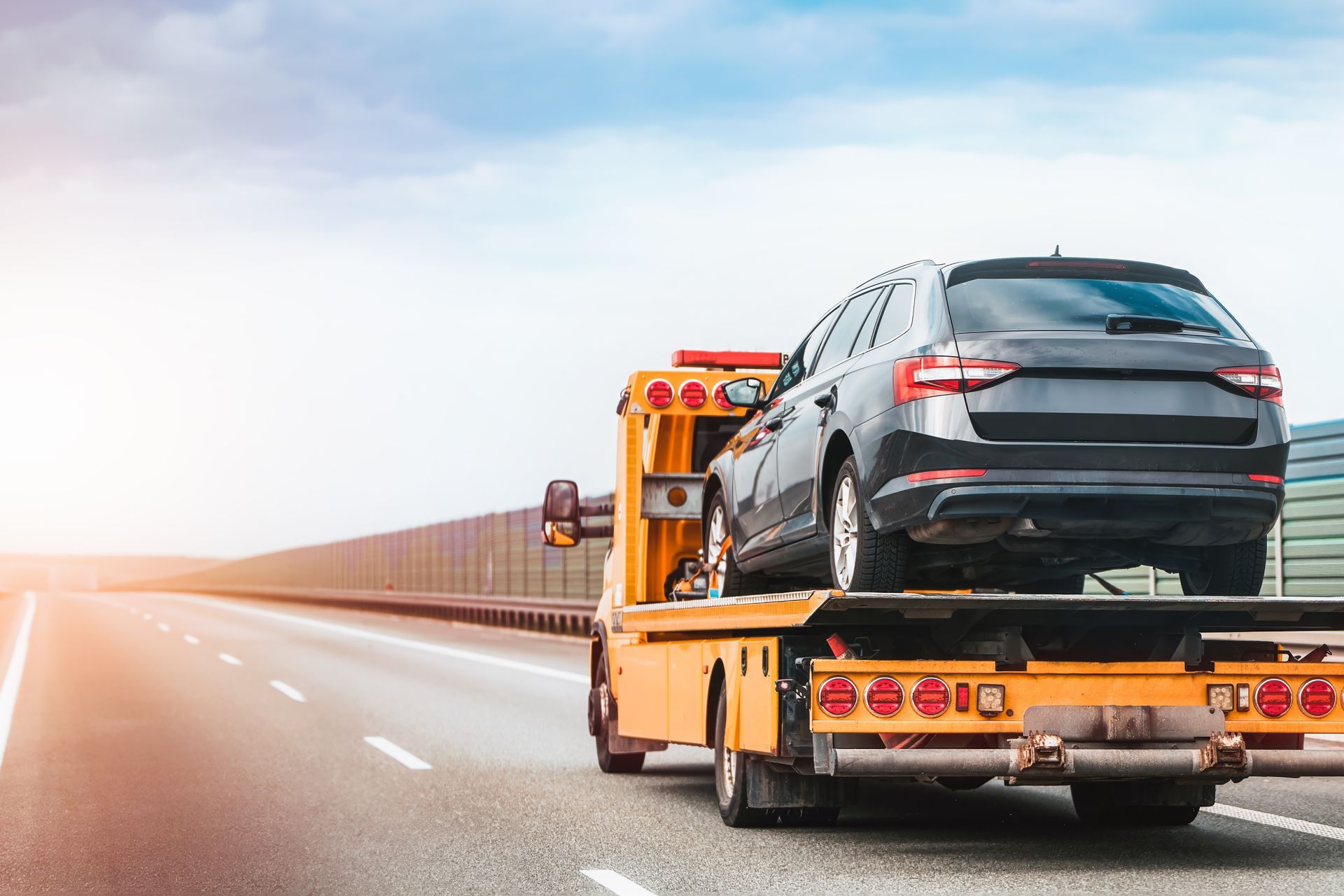 Flatbed tow truck hauling a gray SUV on a Michigan highway.