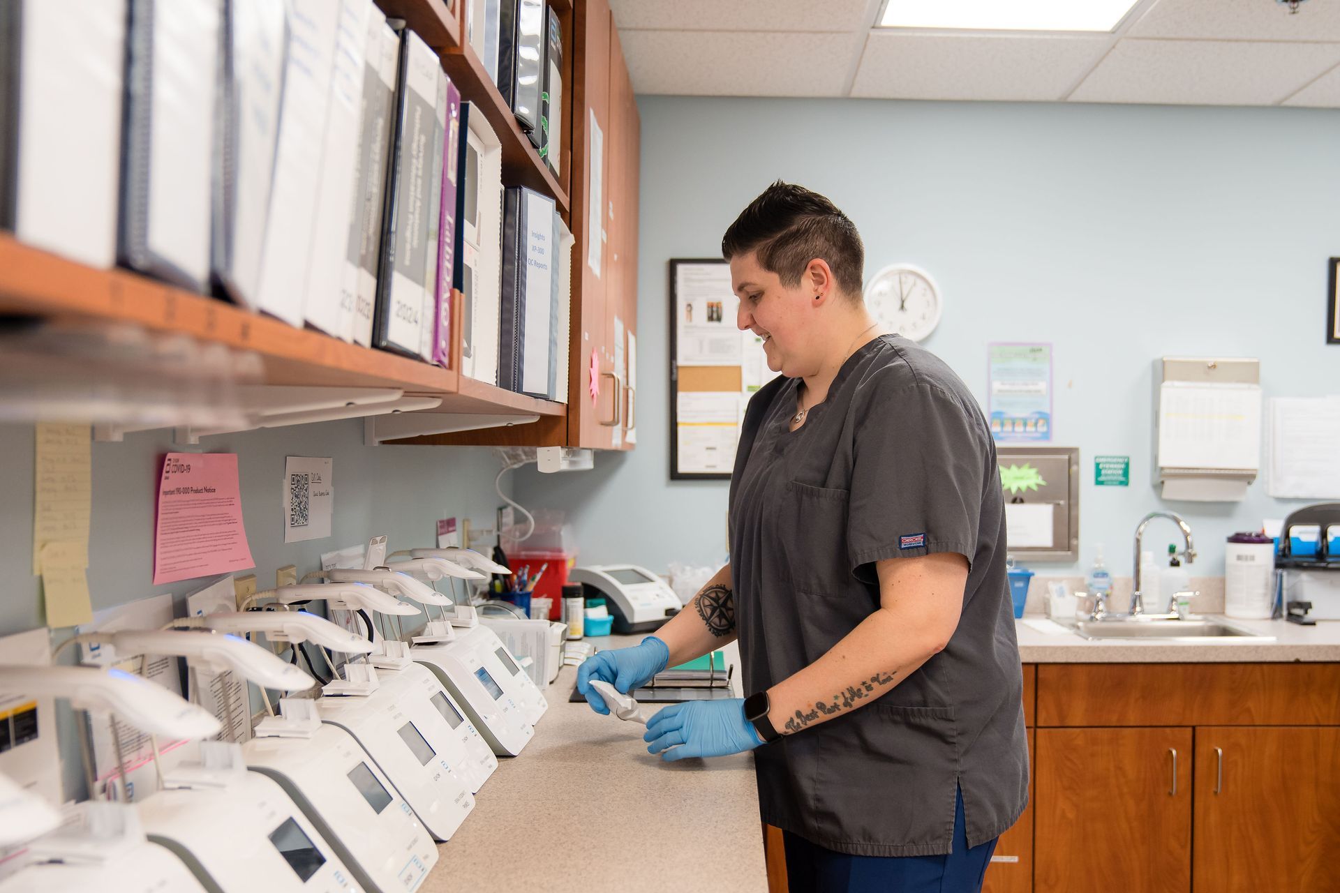 A lab tech in scrubs is working in a lab.
