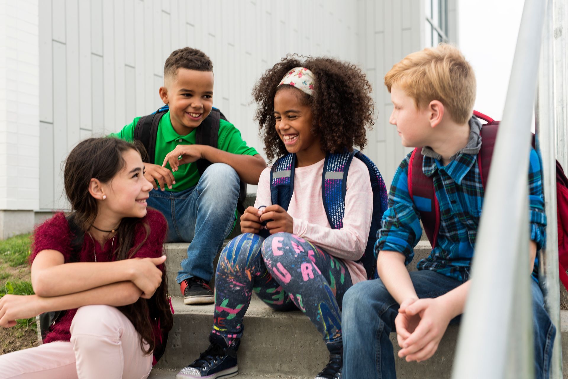 A group of children are sitting on the steps of a school building talking to each other.
