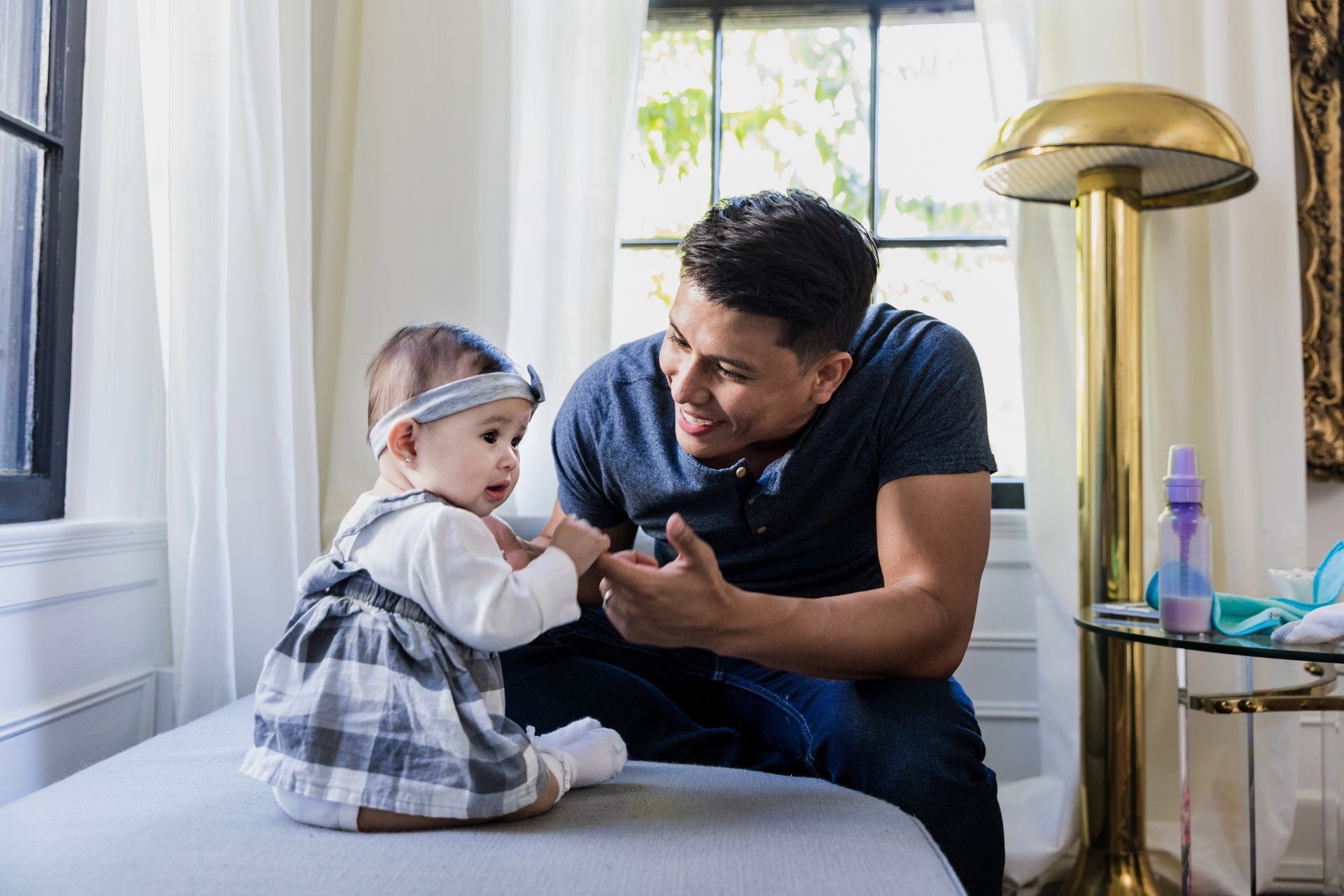A man is sitting on a couch playing with a baby girl.