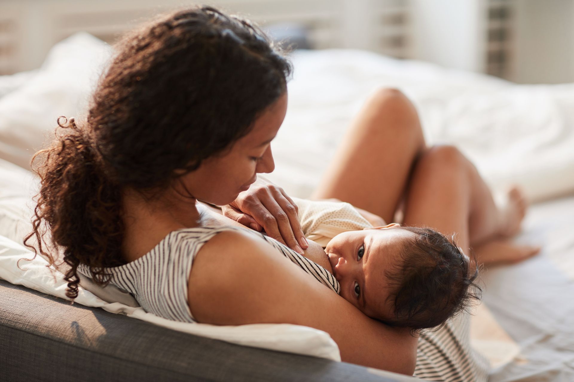 A woman is breastfeeding her baby on a bed.