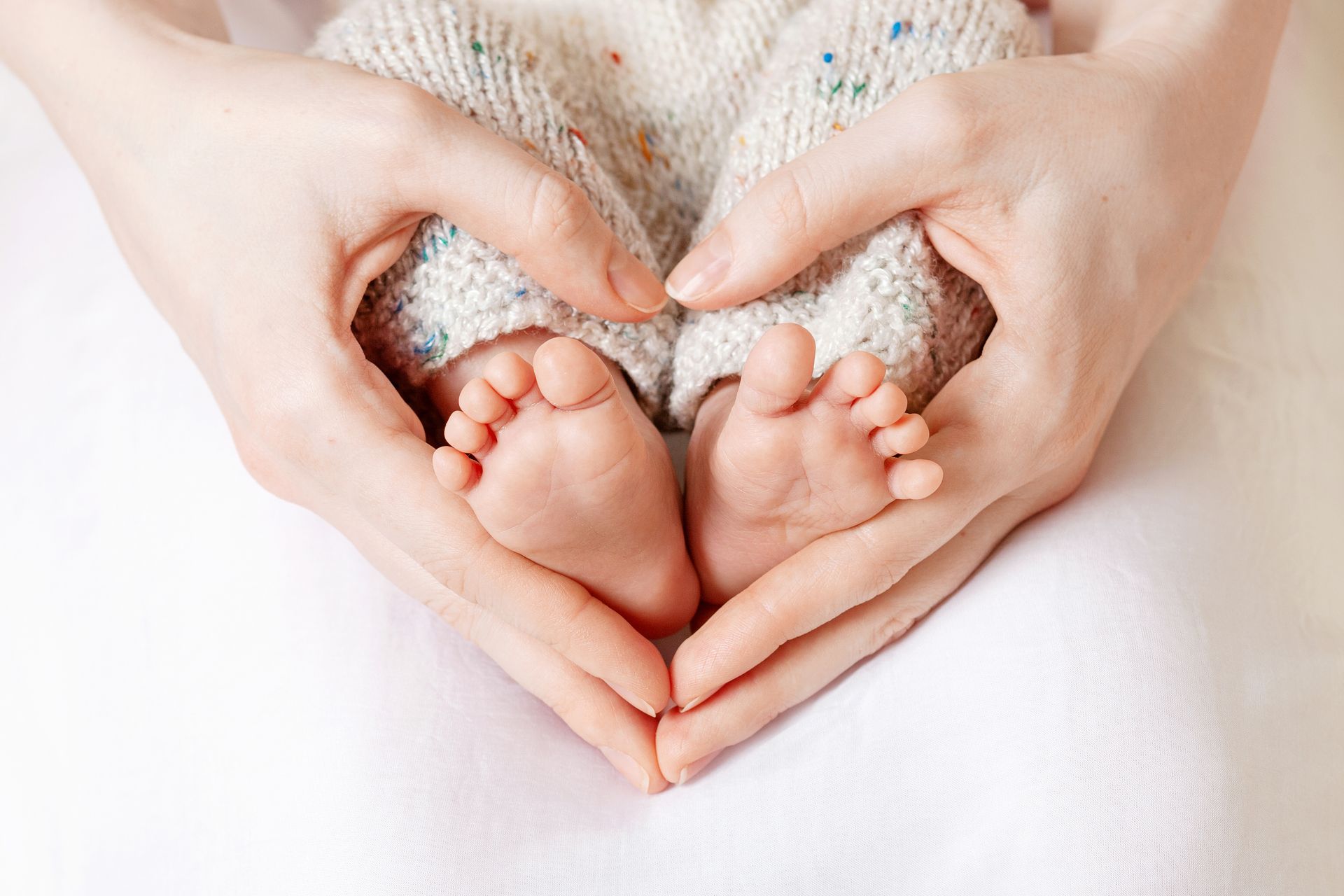Parent cradling the tiny feet of a newborn baby, hands are in a heart shape