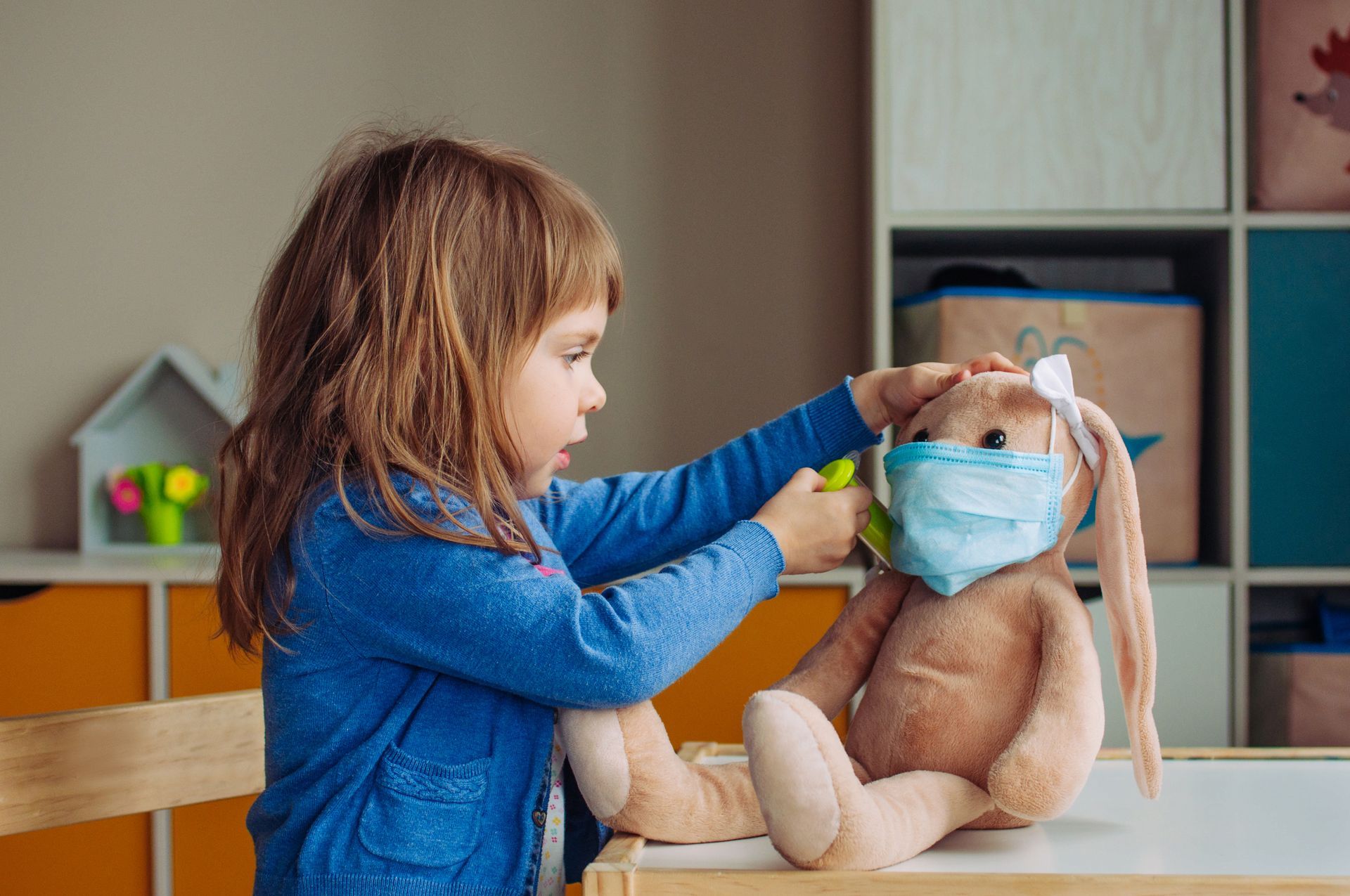 A little girl is putting a mask on a stuffed animal.