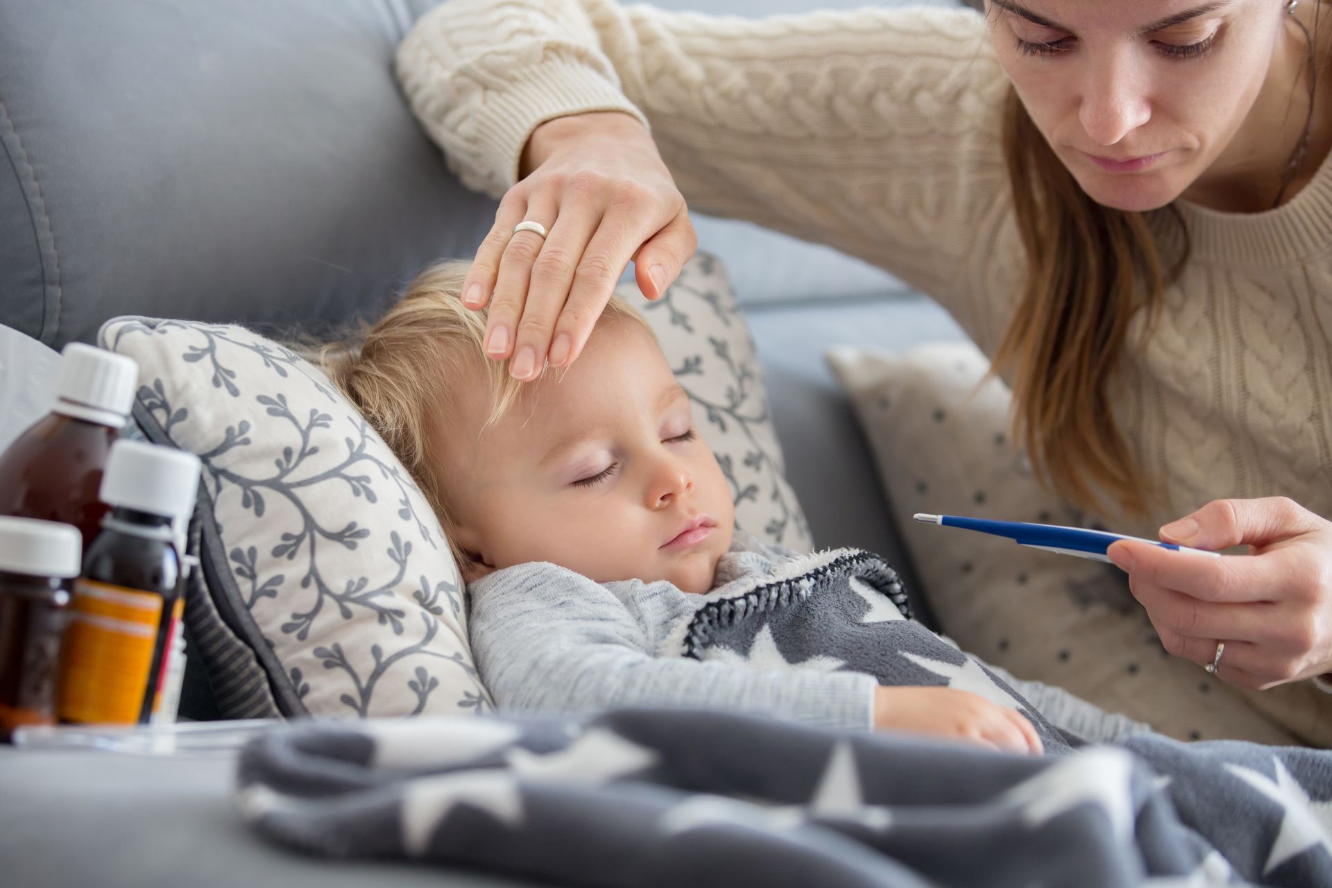 Mom touching the forehead of a sick boy while looking at a thermometer