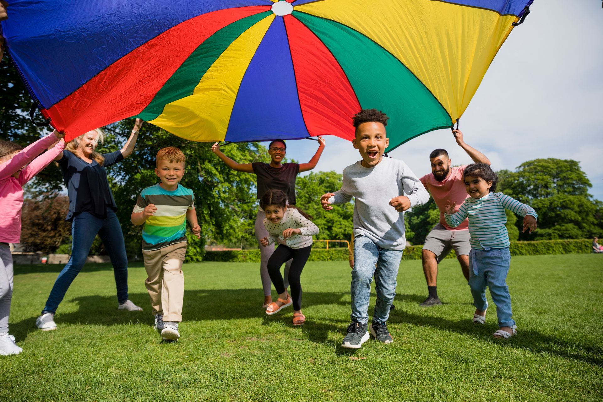 A group of children are playing with a colorful parachute in a park.