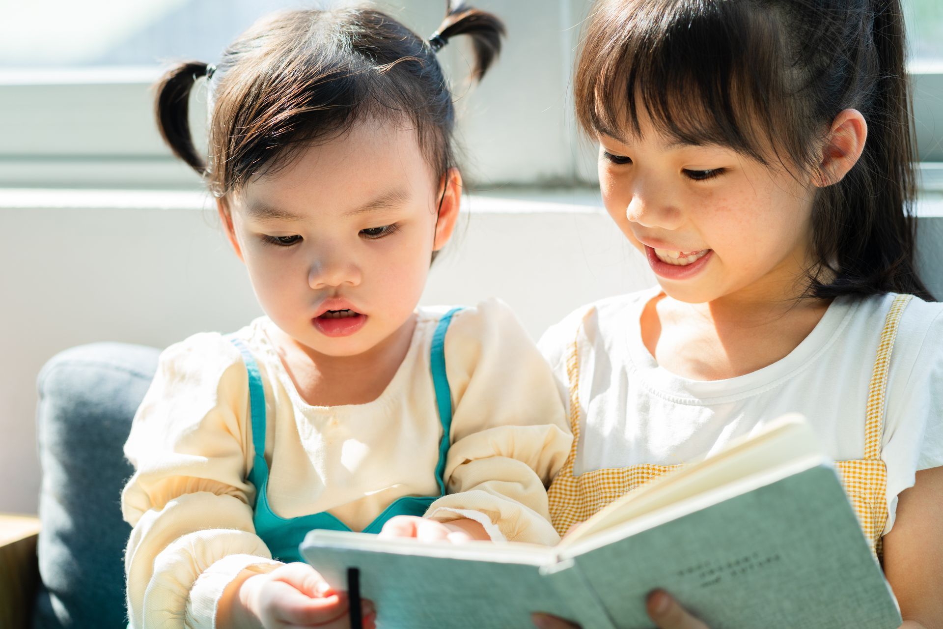 Two little girls are reading a book together.