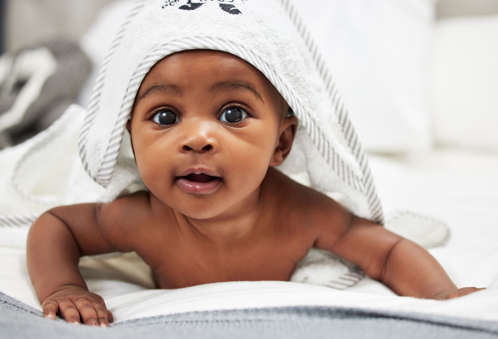A baby is laying on a bed with a towel on his head.