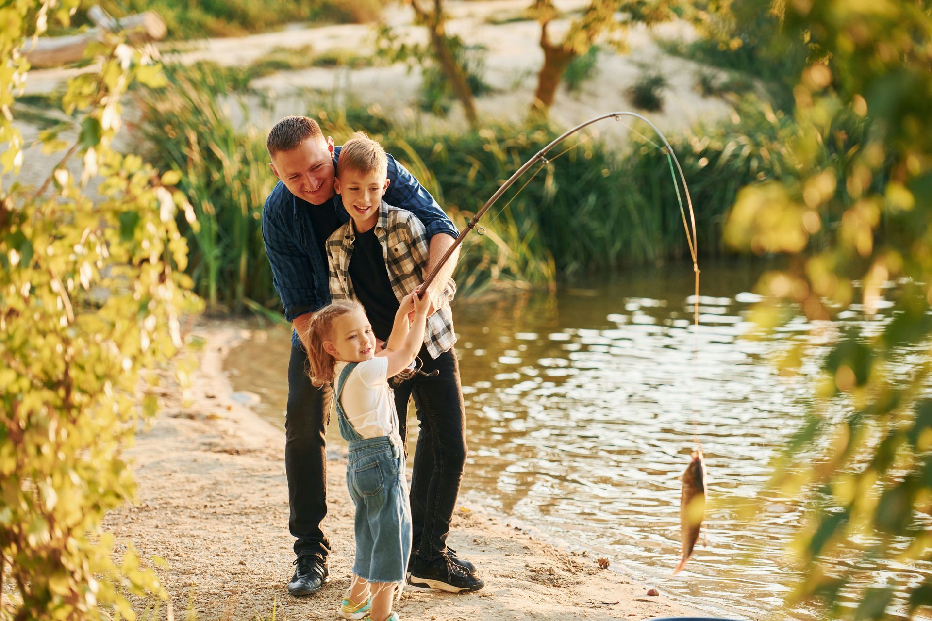 A man and two children are fishing in a lake.