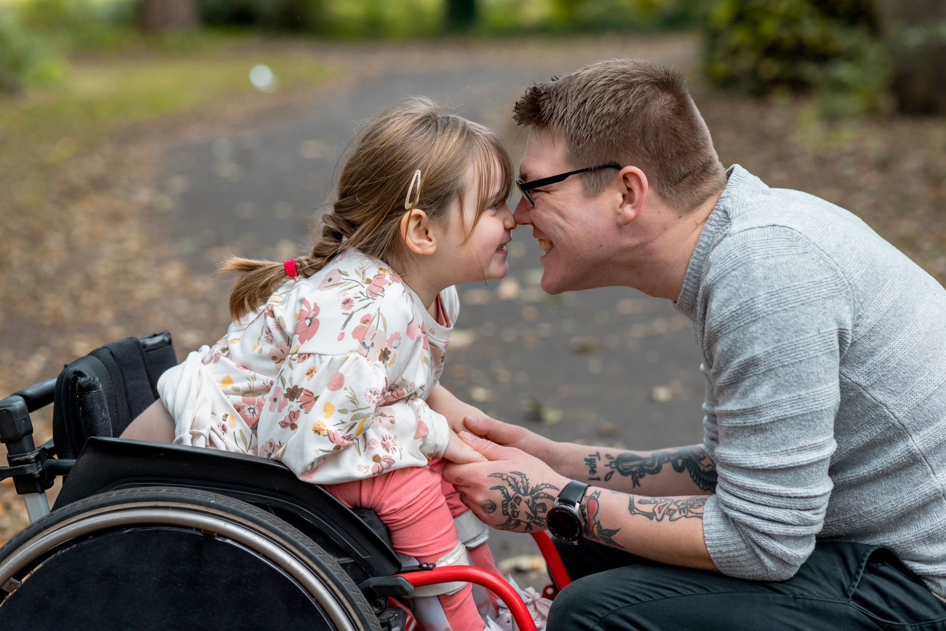 A man and a little girl in a wheelchair are touching noses.
