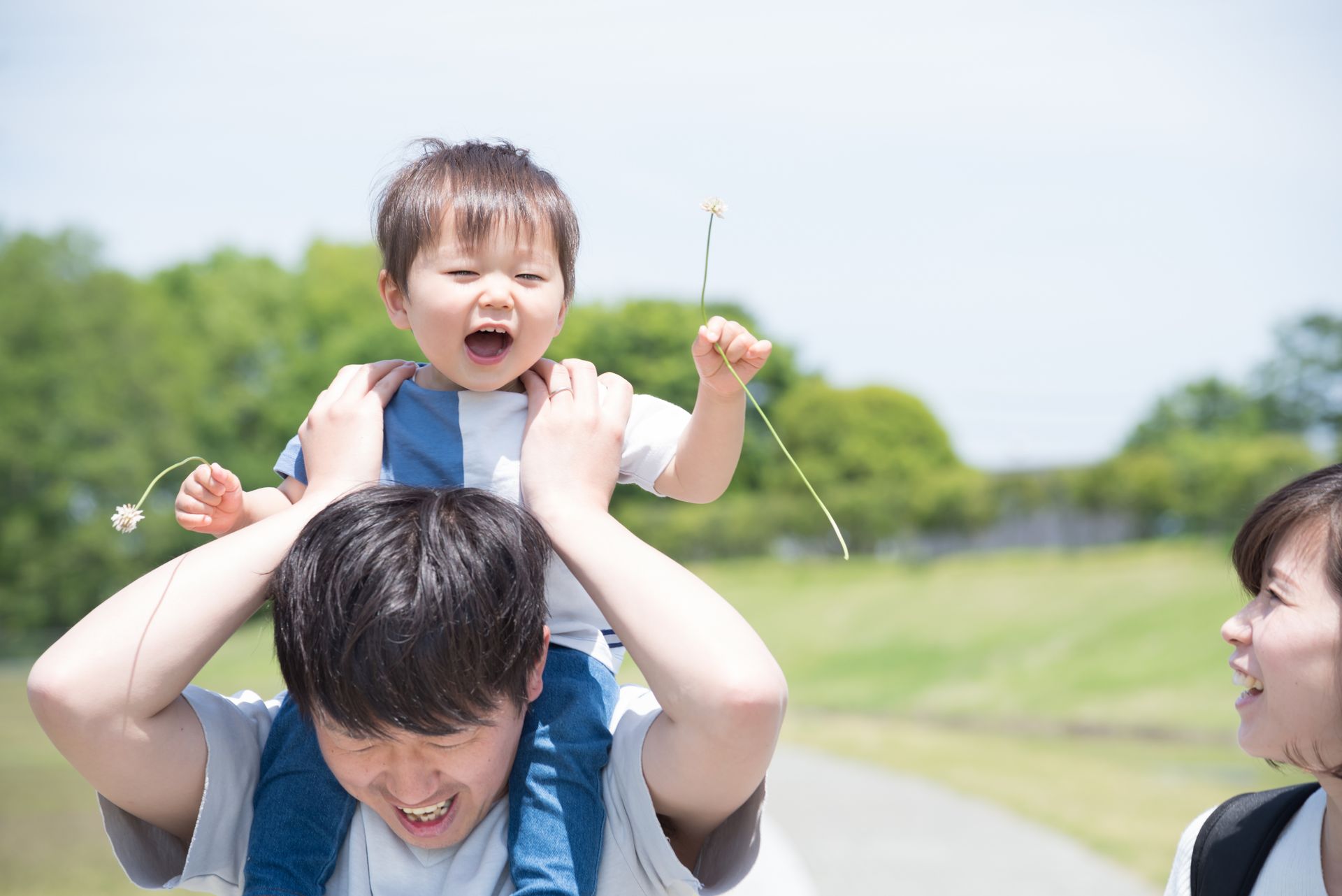 A man is carrying a baby on his shoulders in a park.