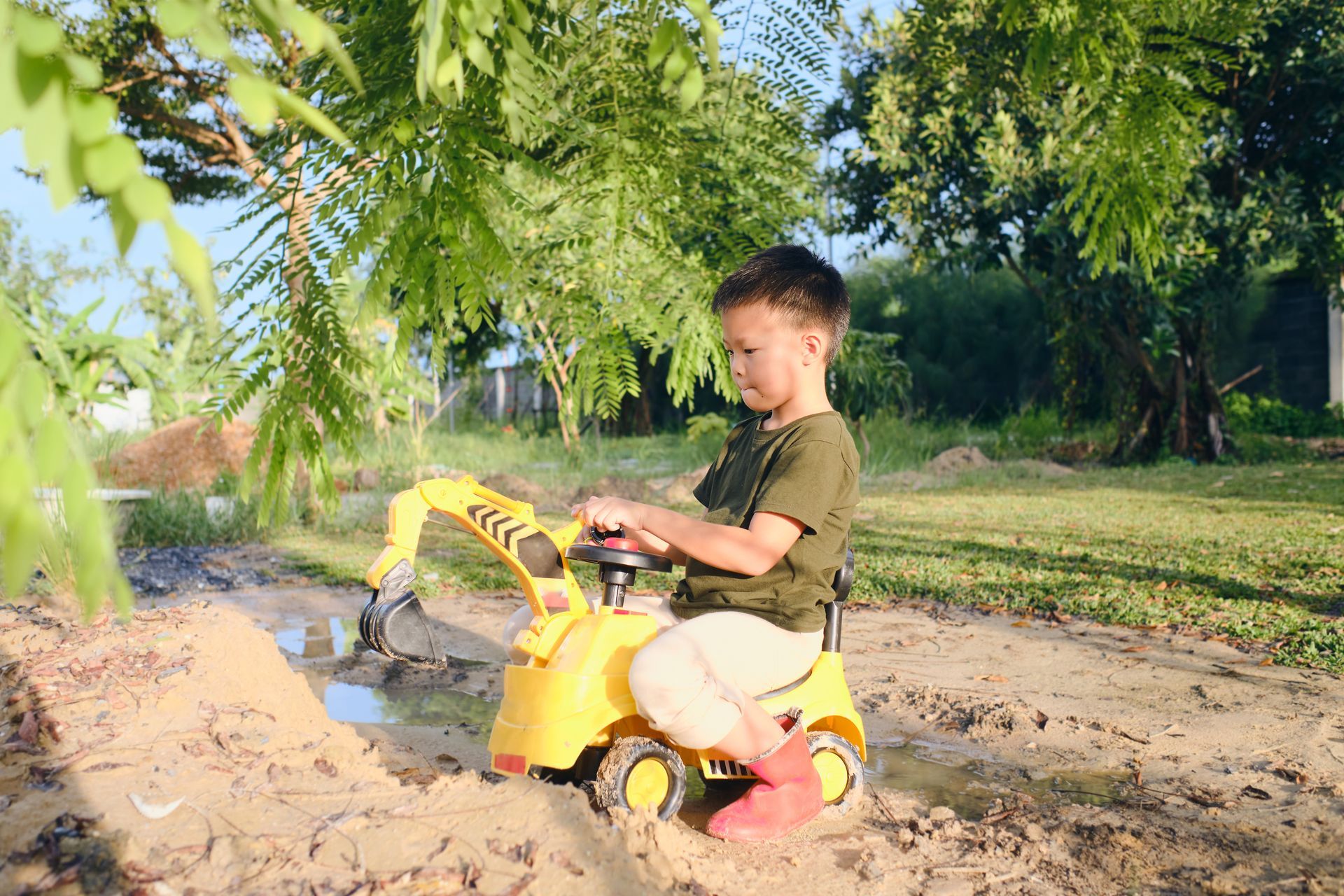 A young boy is playing with a toy excavator in the dirt.