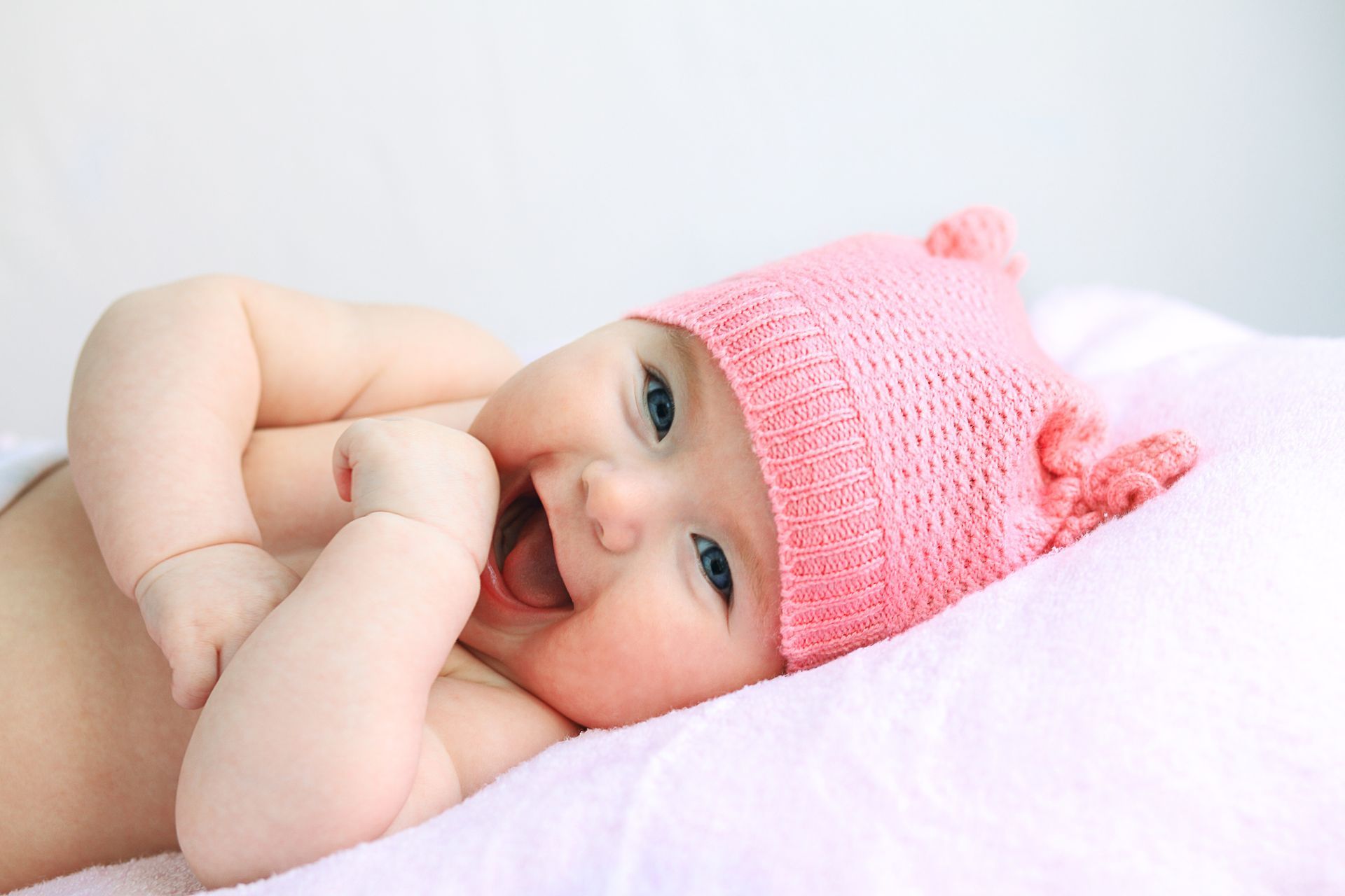 A baby wearing a pink hat is laying on a bed.