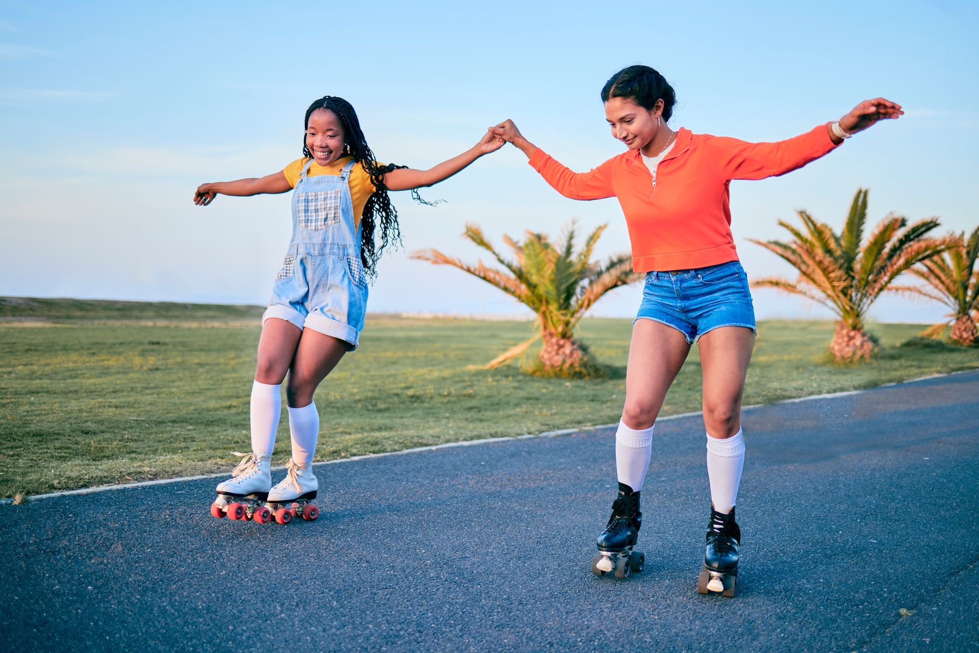 Two women are rollerblading on a road holding hands.