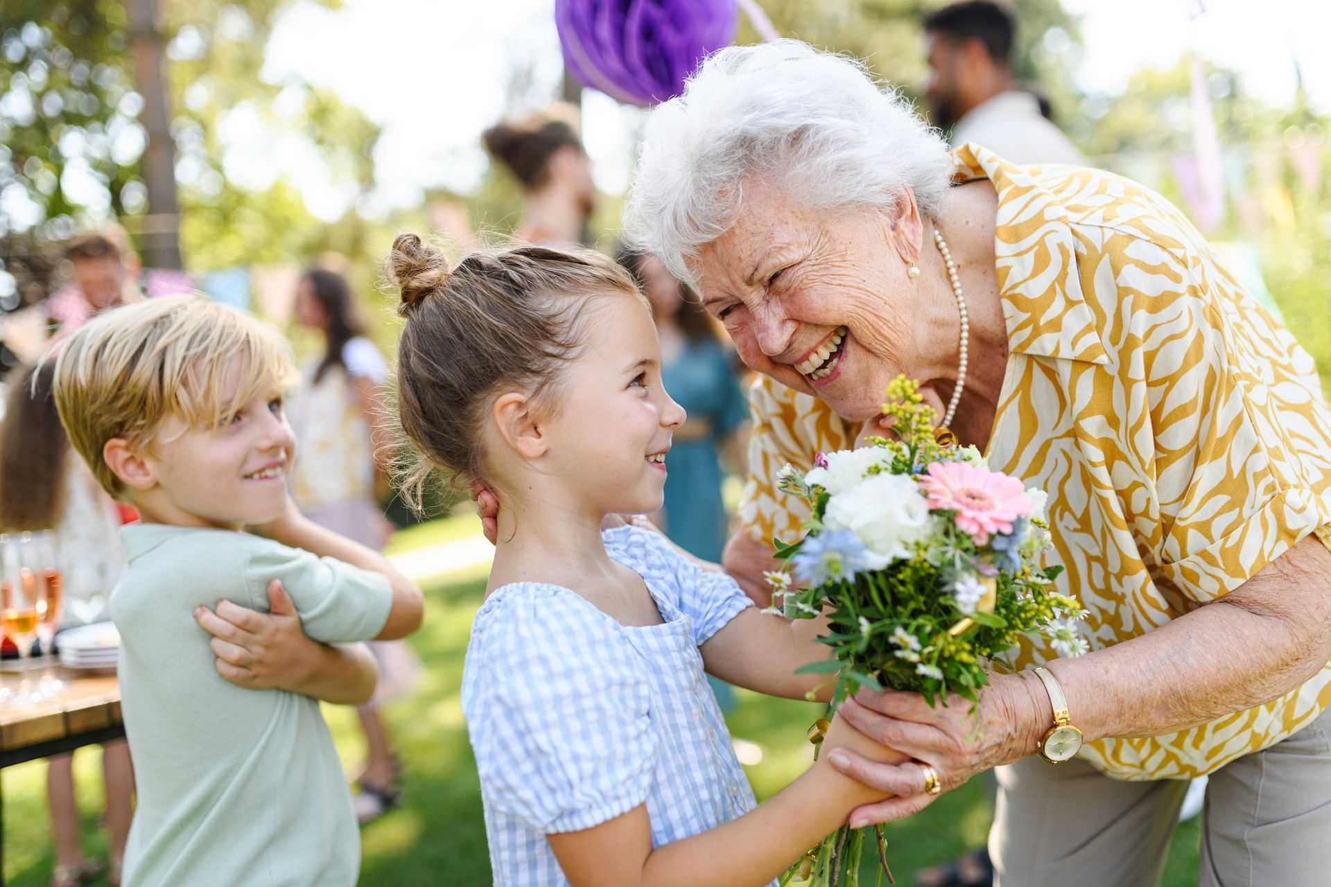 An elderly woman is giving a little girl a bouquet of flowers.