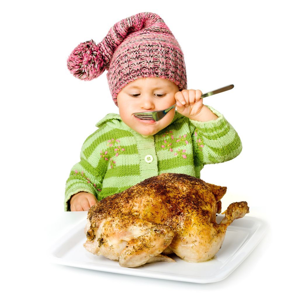 A little girl is eating a roasted chicken with a fork