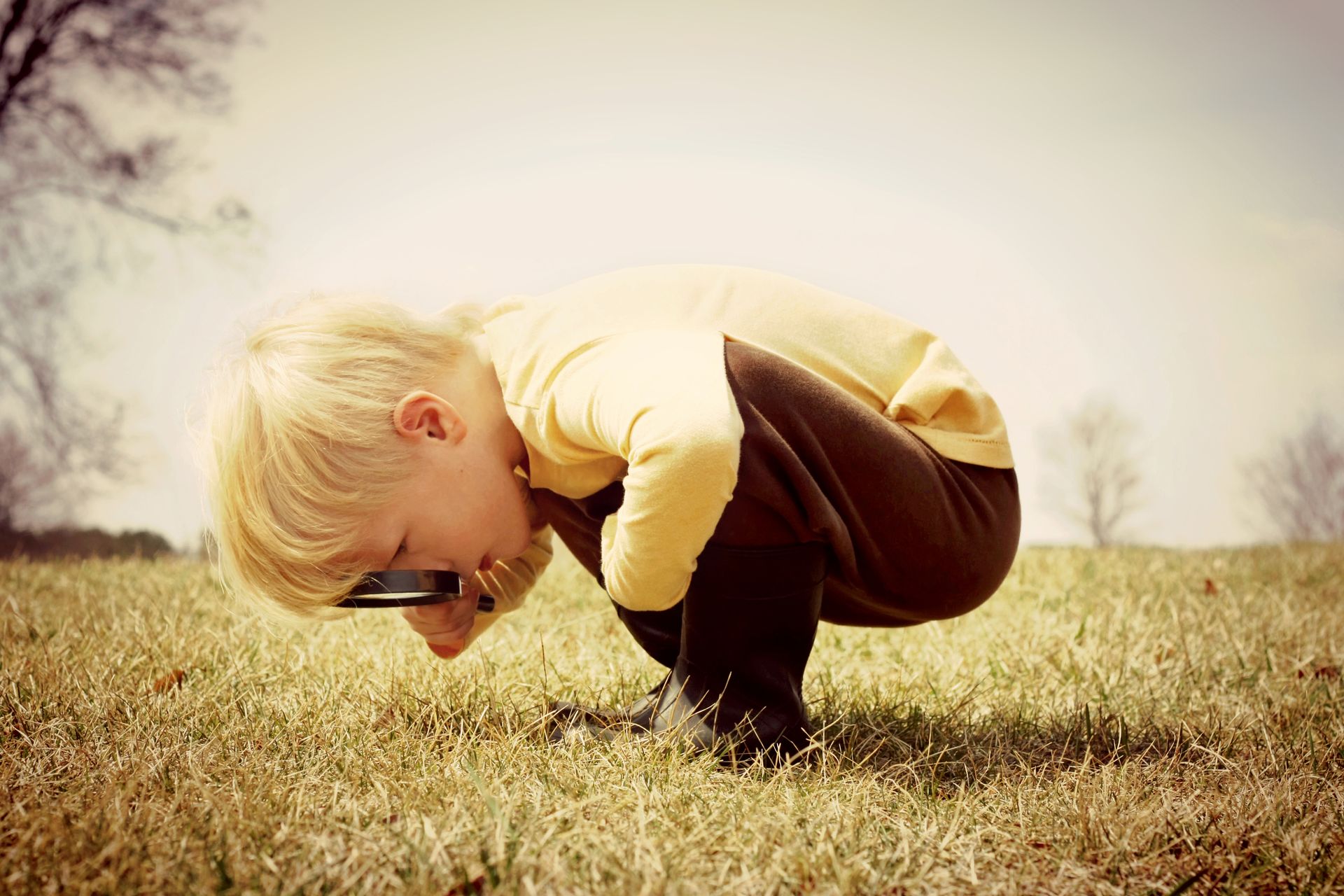 A young boy is looking through a magnifying glass in the grass.