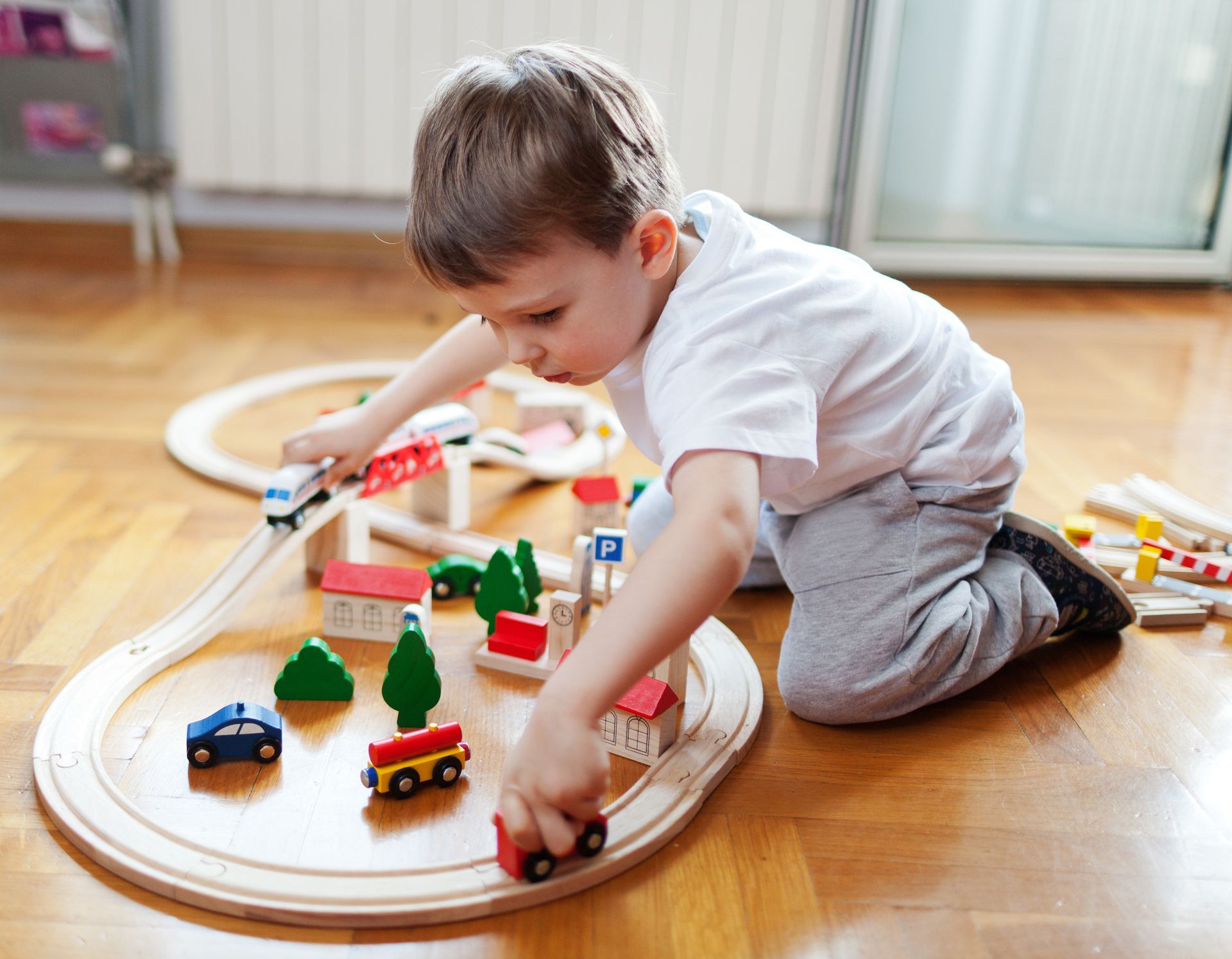 A young boy is playing with a wooden train set on the floor.