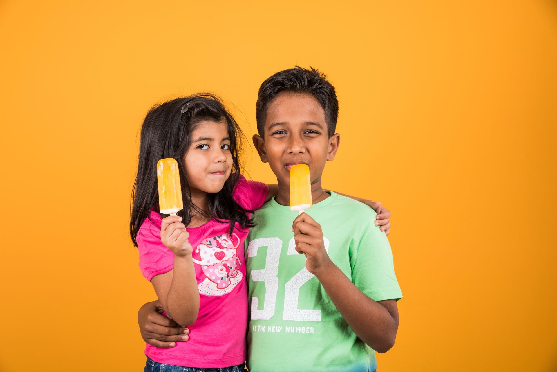 A boy and a girl are eating ice cream on a yellow background.