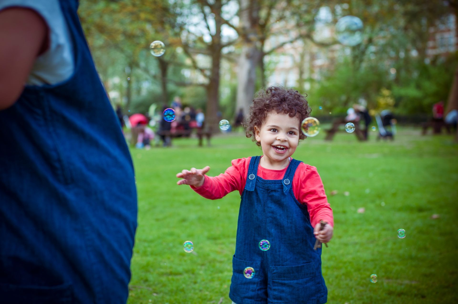 A little girl is playing with soap bubbles in a park.
