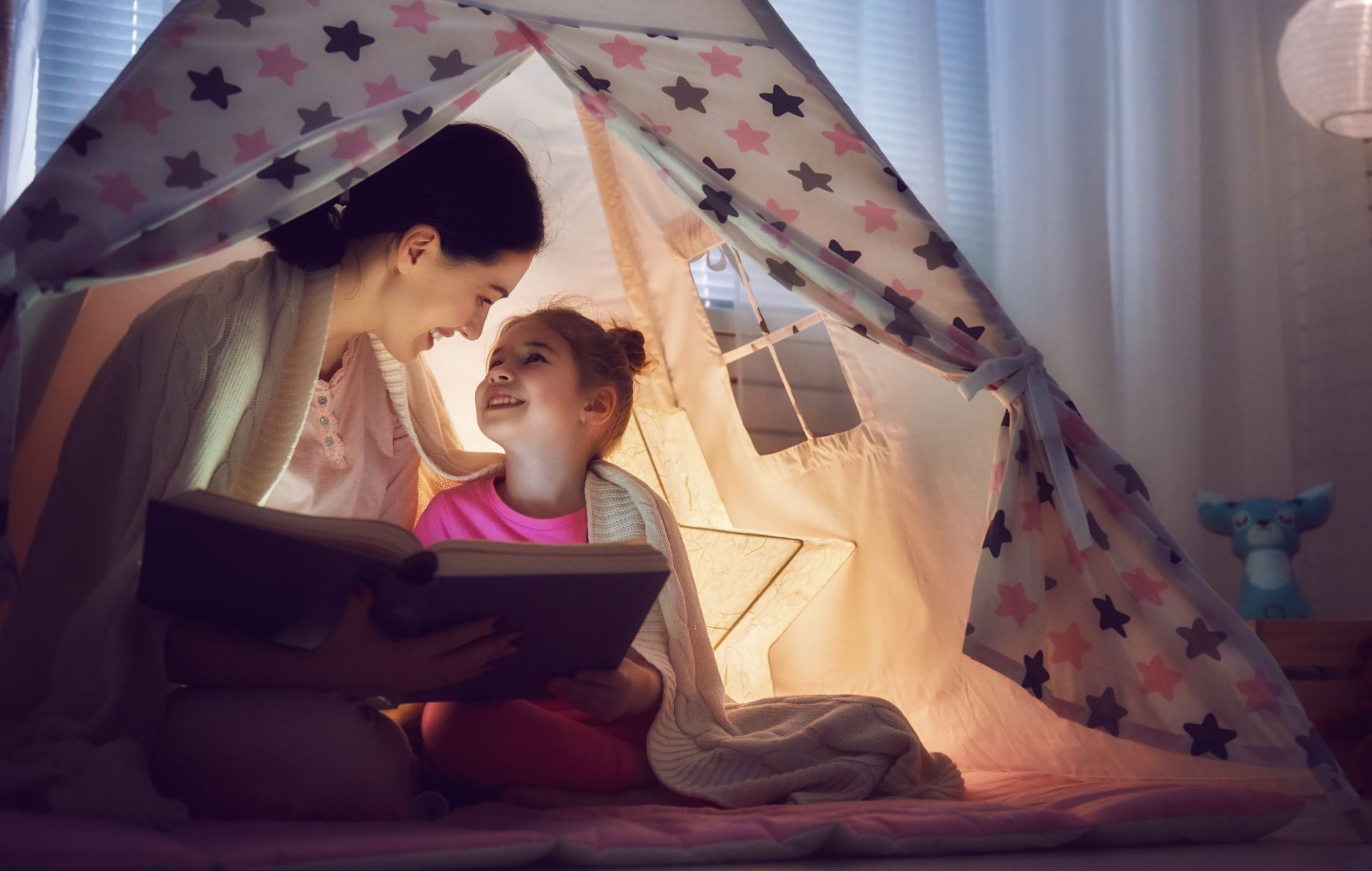 Mom and child reading a book using a flashlight in a homemade tent