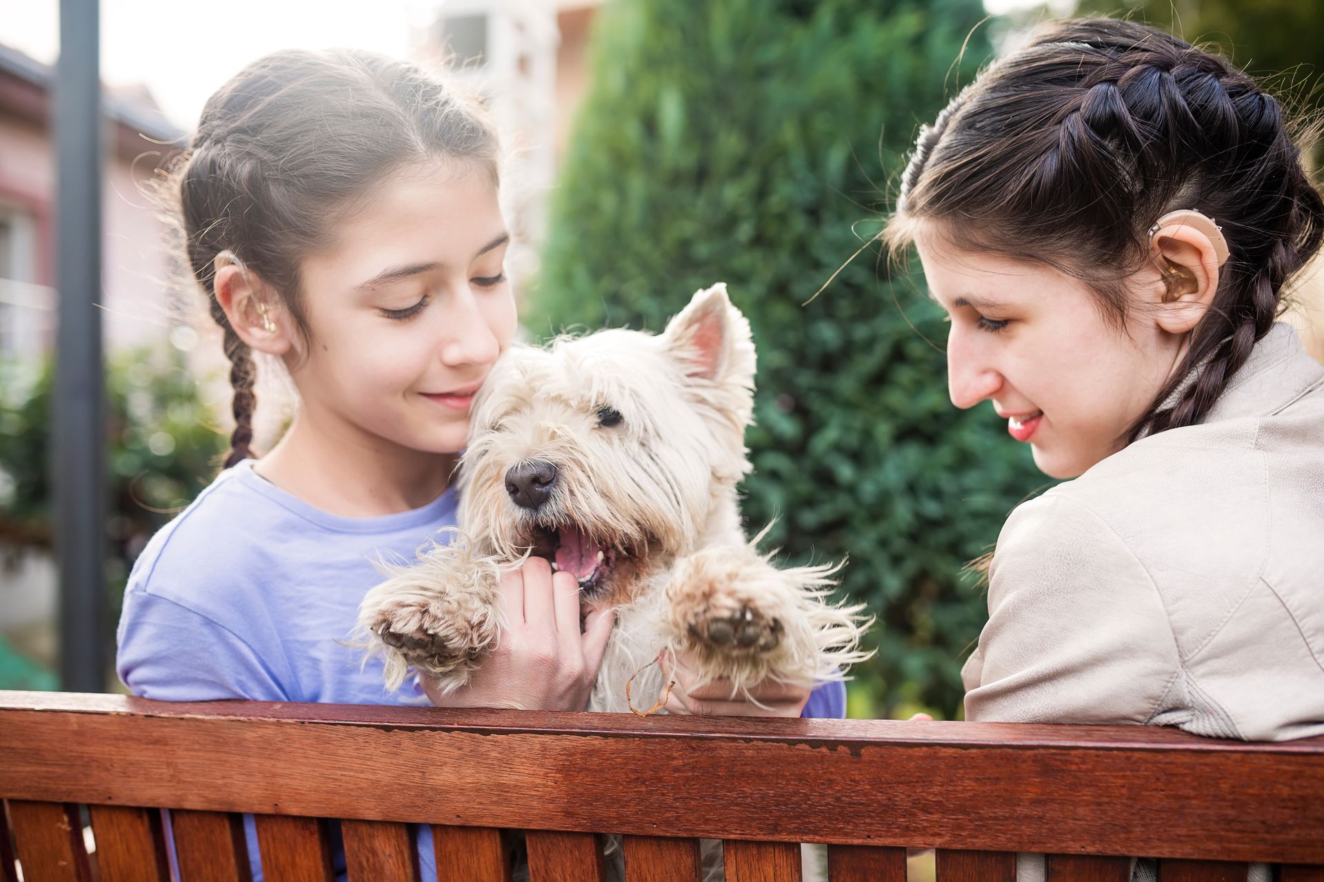 Two girls are sitting on a bench petting a small dog.