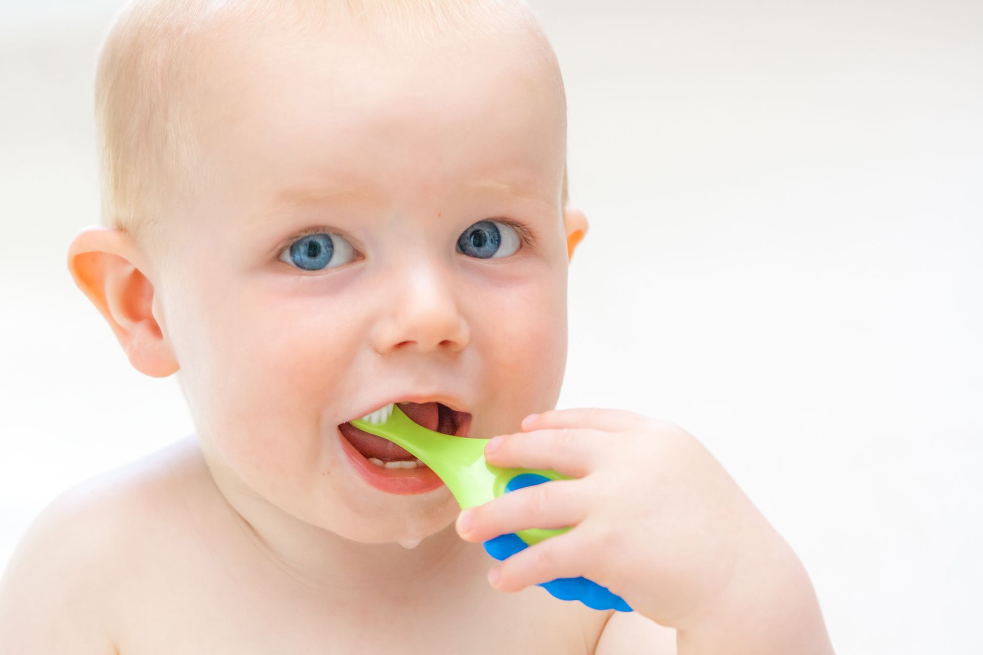 A baby is brushing his teeth with a green toothbrush.