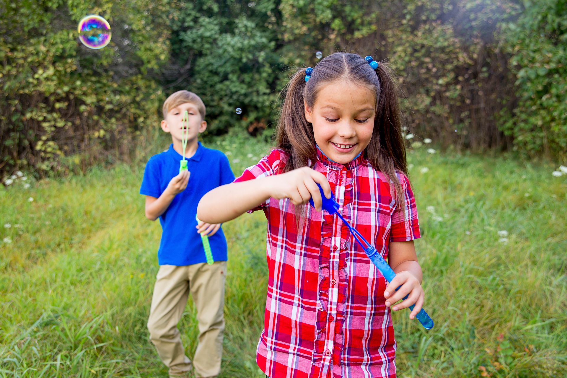 A boy and a girl are blowing soap bubbles in a field.