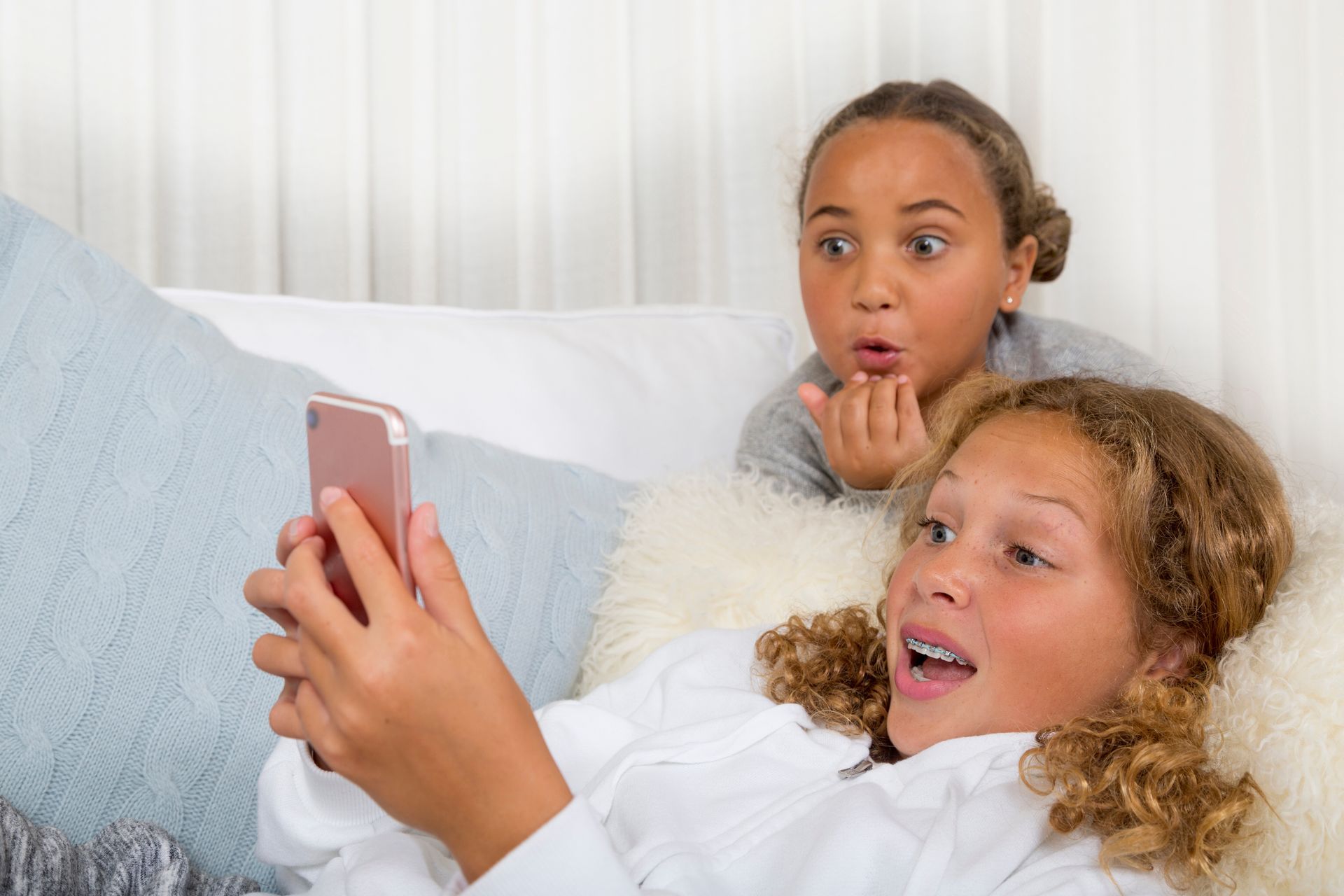 Two young girls are laying on a bed looking at a cell phone.
