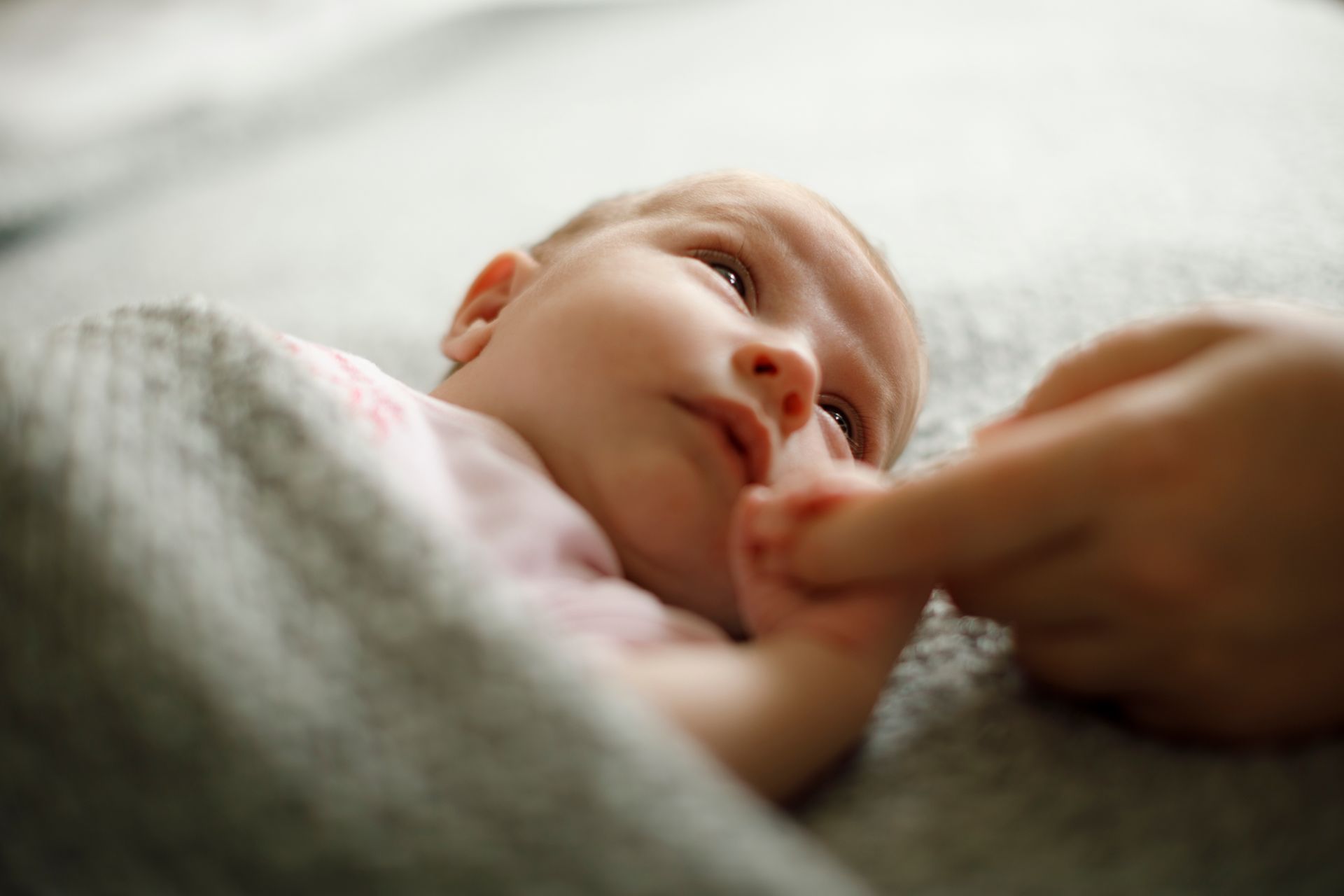 A baby is laying on a bed with a person holding its hand.
