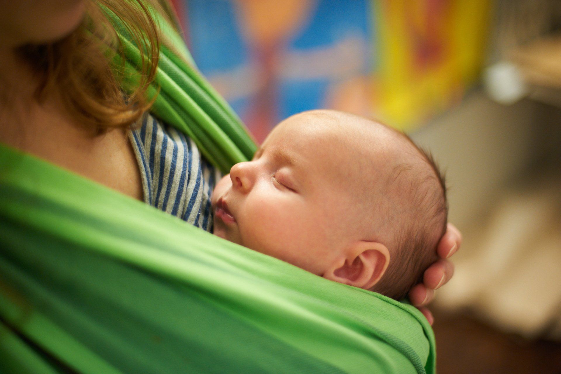 A woman is holding a baby in a green sling.