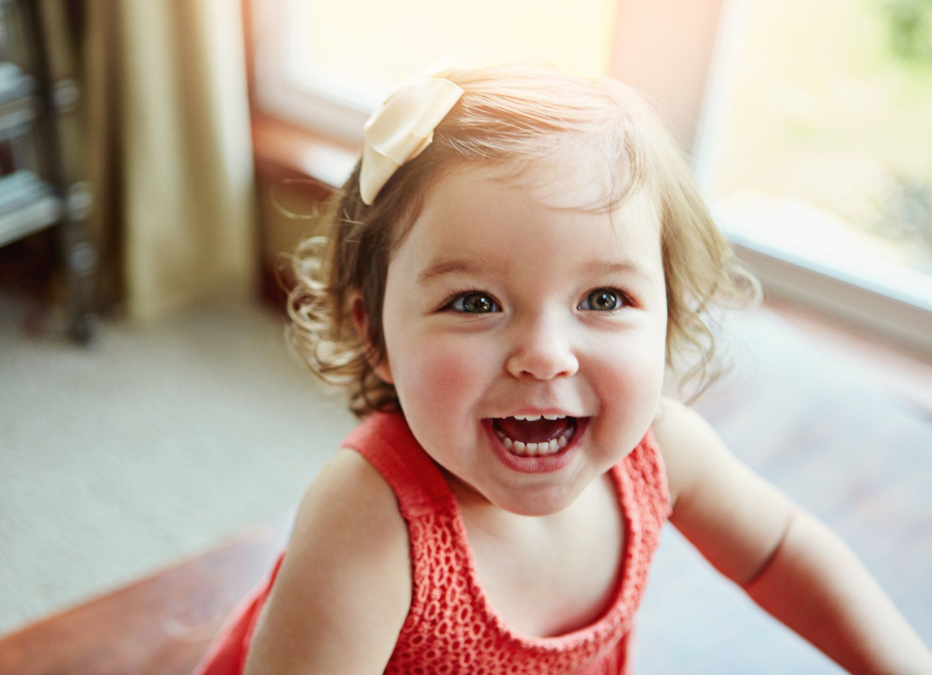 A little girl is smiling while sitting on the floor in front of a window.