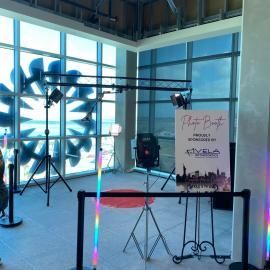 Indoor event setup with lighting rig, neon floor lights, and a sign on an easel in a modern lobby