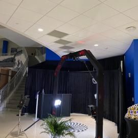 Indoor event space with a camera crane, stage curtains, lights, and a potted plant
