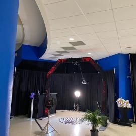 Empty event space with blue walls, black curtains, a red-black arch, and a bright spotlight in the center