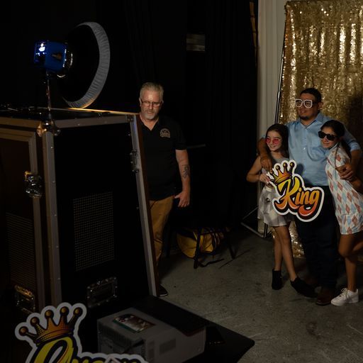 People posing beside a large photo booth with a gold “King” sign in a dark event space