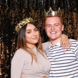 Two people smiling in crowns posing in front of a gold sequin backdrop
