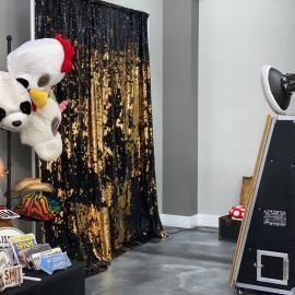 Photo booth with black-and-gold curtain, large plush bear, and props in a decorated indoor corner