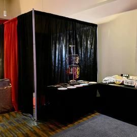Black-draped display booth with tables, plates, and stacked bottles at an indoor event