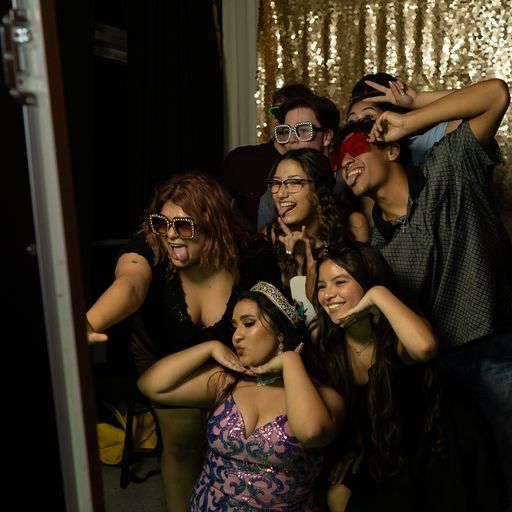 Five friends posing playfully in costumes and oversized glasses for a photo booth picture