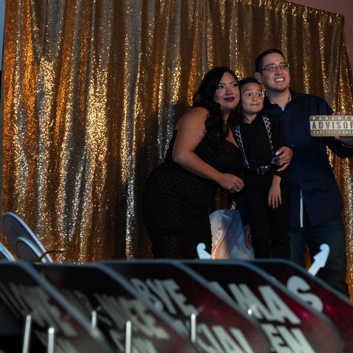 Three people posing in front of a gold backdrop at a photo booth event