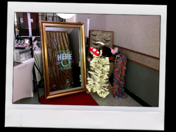A framed mirror leaning by a corner, reflecting a store display with colorful clothing and a mushroom decoration