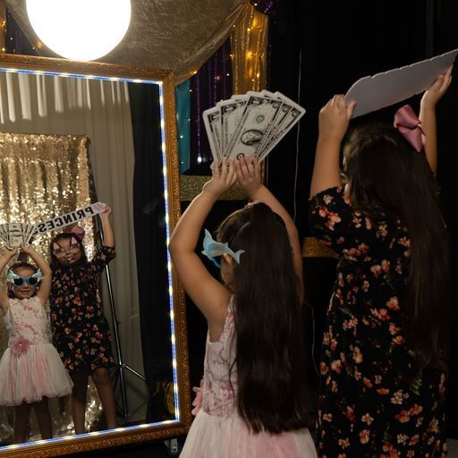 Girls in dresses posing with props in a decorated photo booth with gold curtains and lights