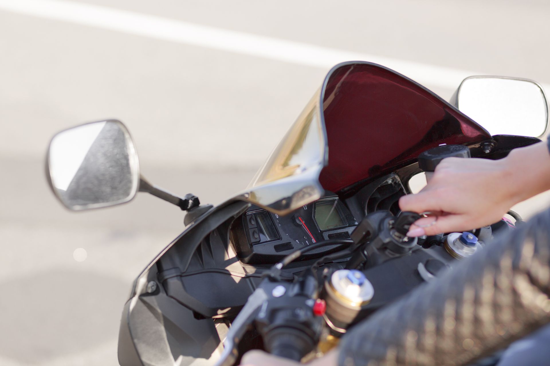 Person starting a black motorcycle. Close-up view of hands turning the ignition key. Sunny outdoor setting.