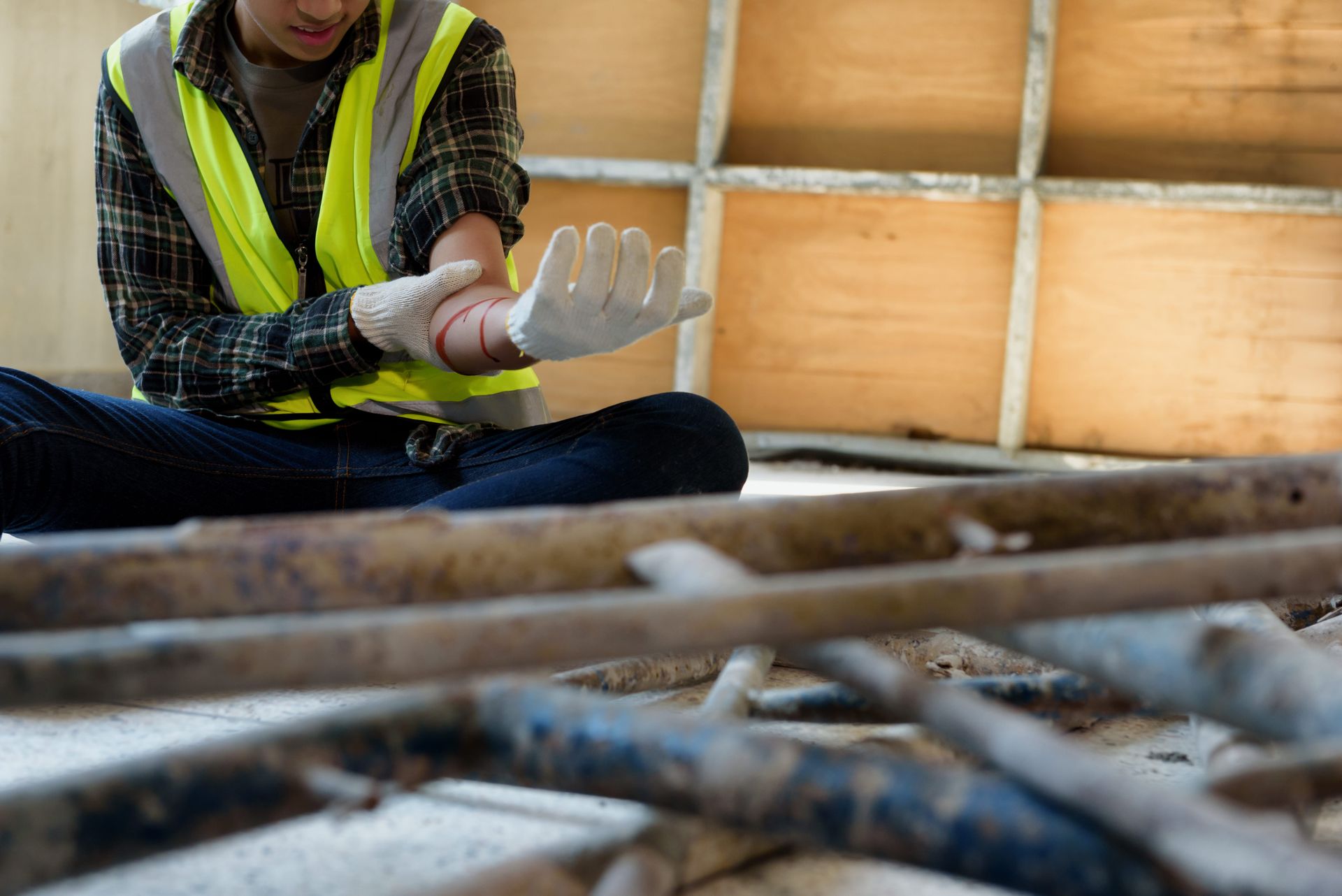Worker in a reflective vest putting on gloves at a construction site with wooden framing and metal rods in the foreground