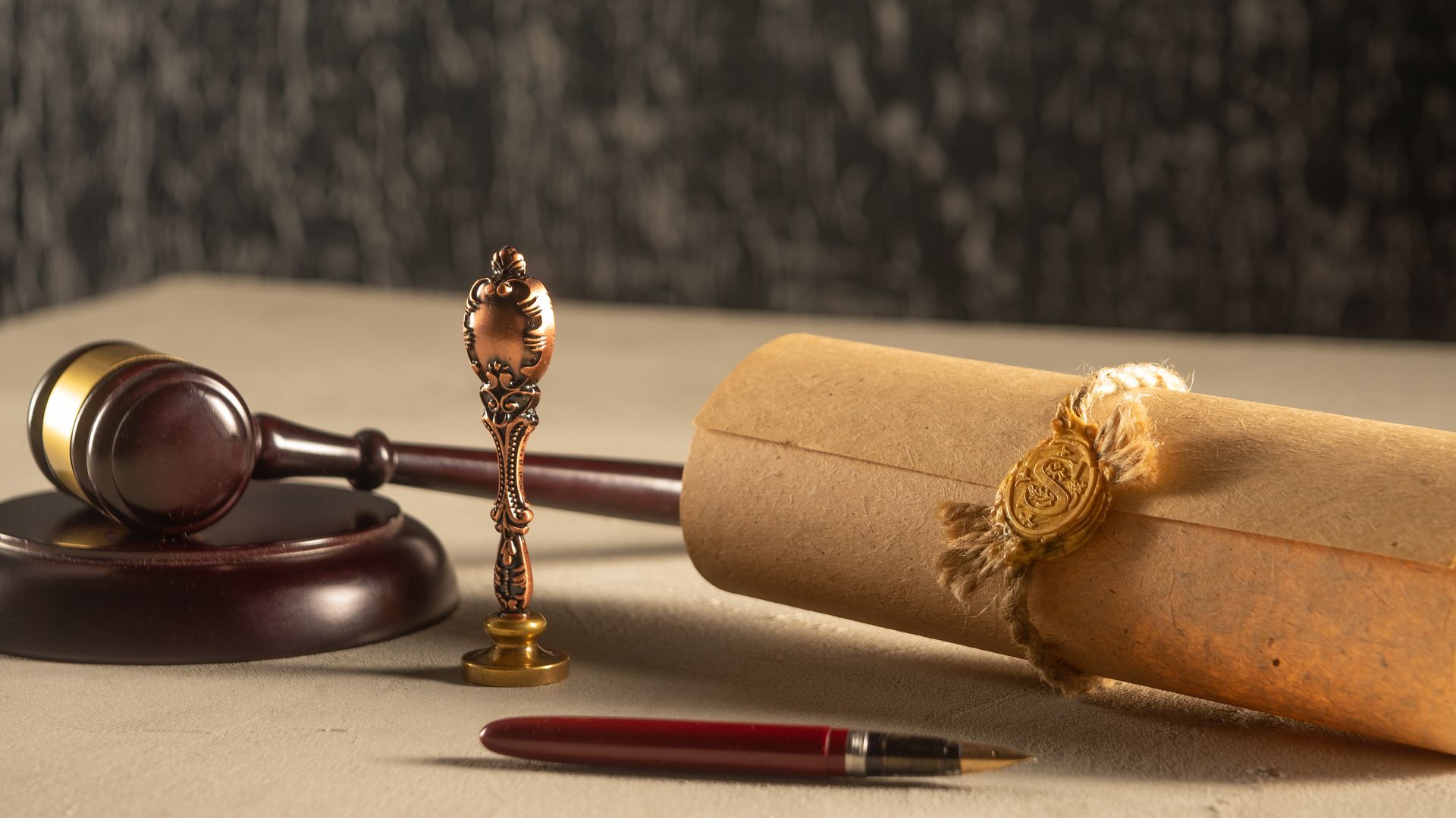 Gavel, scroll with seal, and pen on a light-colored surface, suggesting legal or official documentation.