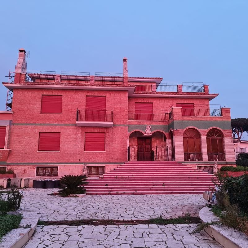 Grande casa rosa a due piani con scala frontale e portico ad arco al crepuscolo